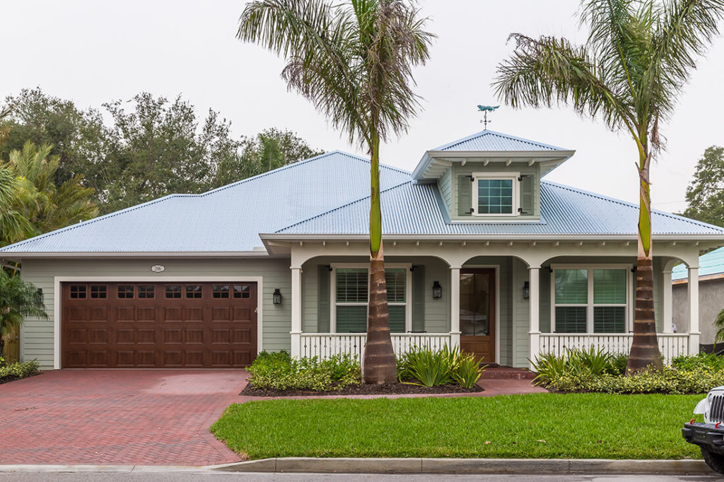 A traditional Florida home with palm trees in the front yard features a paver driveway, two-car garage, fiber cement siding, and a standing seam metal roof.