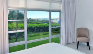 Large aluminum window in bedroom with view of lush green backyard