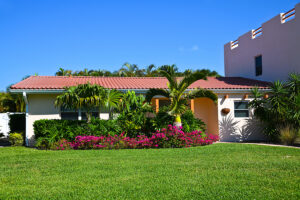 A beautiful Florida home features a Spanish tile roofing system and has a green lawn with palm trees out front.