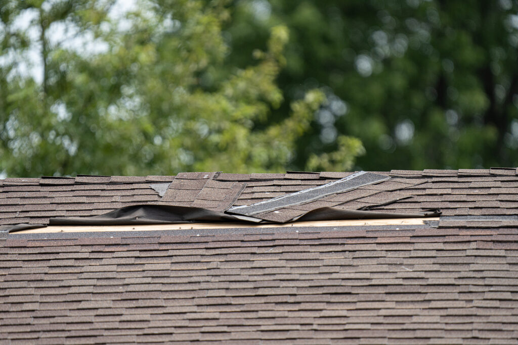 A brown shingle roof with shingles torn off due to strong winds.