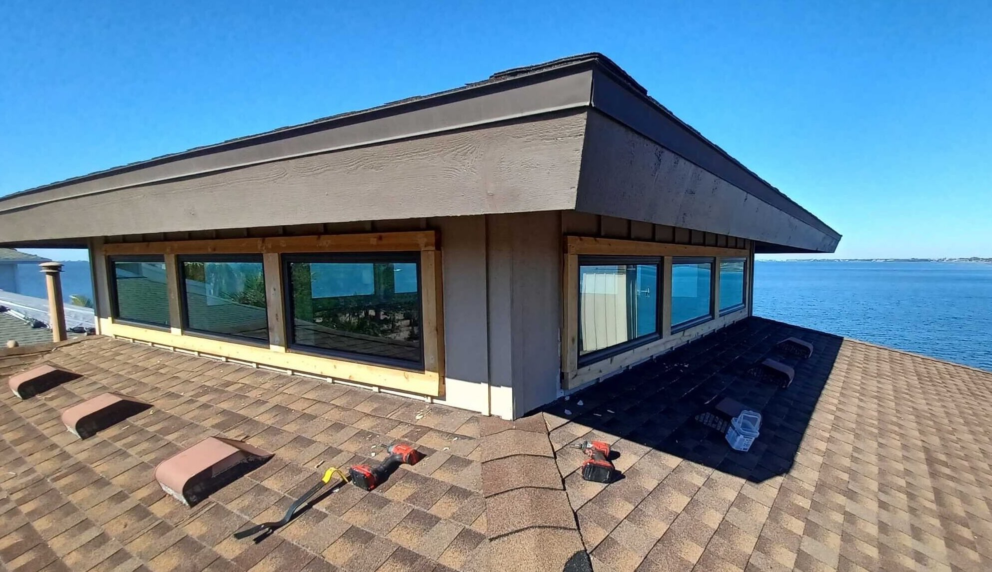 An asphalt roof for a waterfront house is pictured with drills and other roofing tools. 
